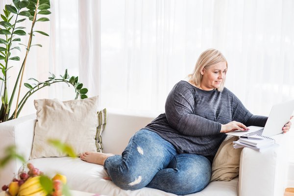 Woman sits on couch with laptop