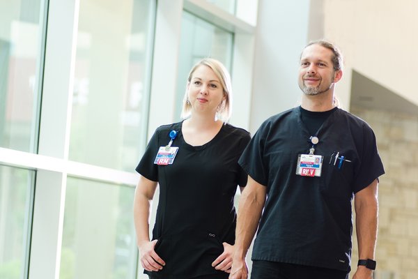 Two CoxHealth employees wearing black scrubs stand next to each other and smile