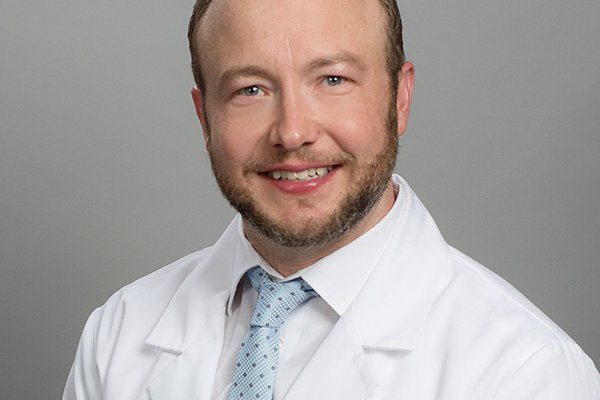 A head shot of Dustin Bartlett shows him in a white coat.