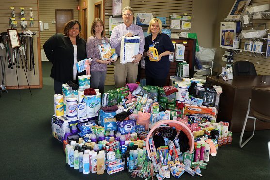 Four people posing with food and toys that were donated