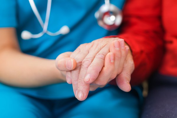 A health care worker holds a patient's hand.