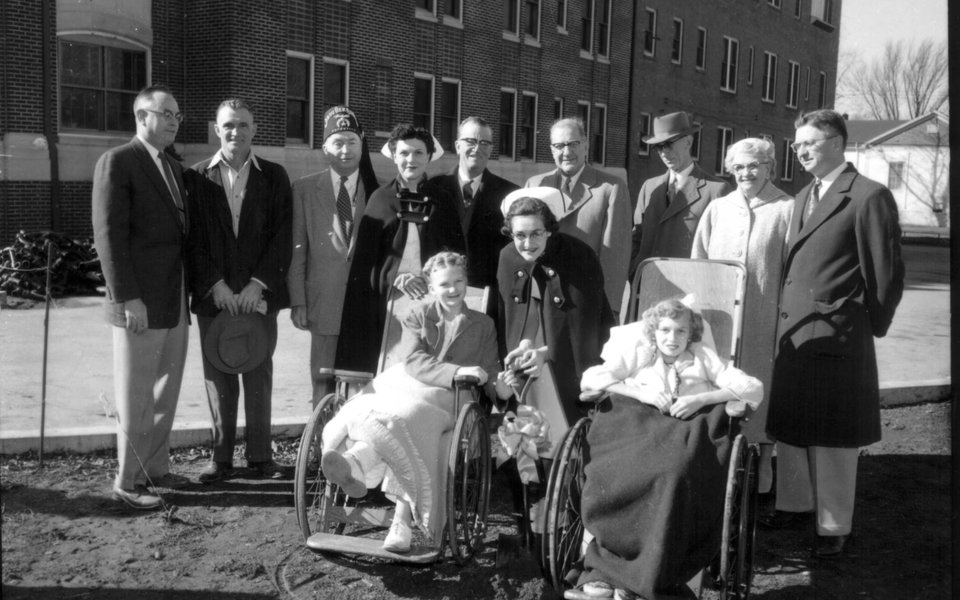 A historic photo of a group of people standing around polio patients in wheelchairs at CoxHealth
