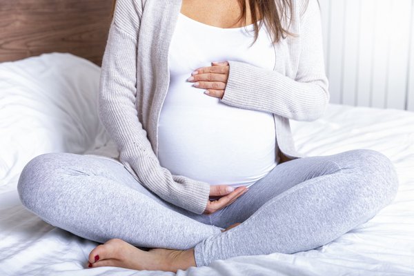 A pregnant woman sits on a bed.