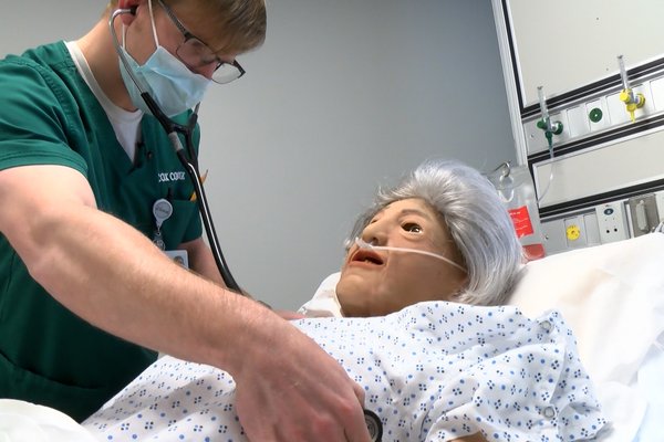 Cox College student checks on elderly manikin patient in simulation lab