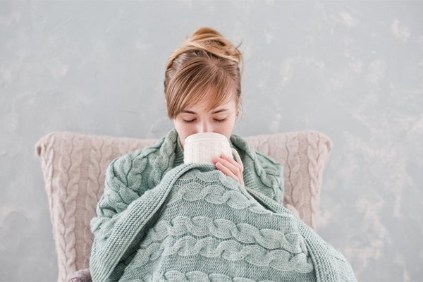 Woman covers up in blanket while drinking out of mug.